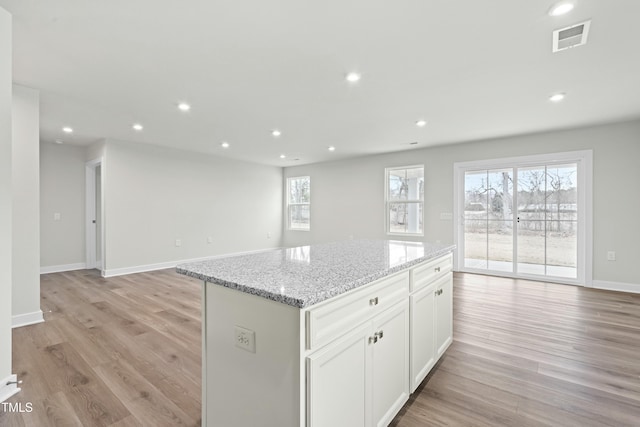 kitchen with light wood-style floors, light stone countertops, a wealth of natural light, visible vents, and a kitchen island
