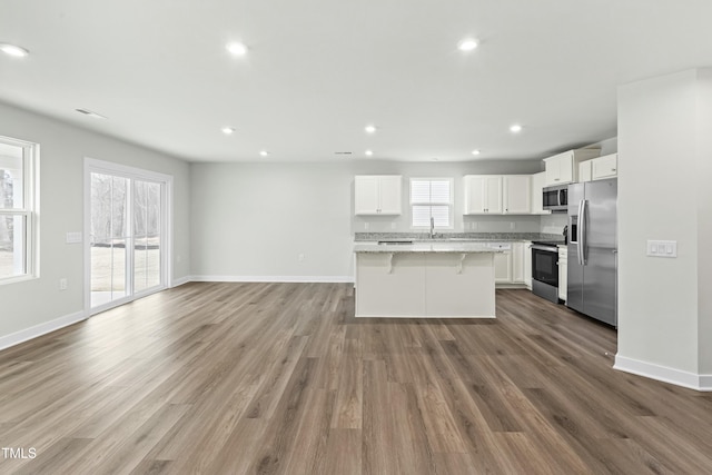 kitchen featuring open floor plan, appliances with stainless steel finishes, a kitchen bar, a kitchen island, and light stone counters