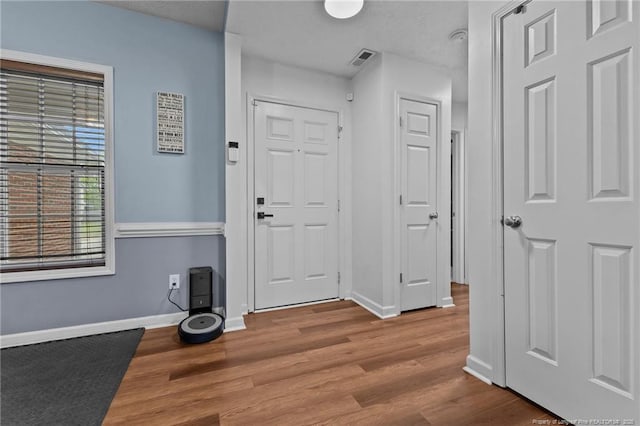 foyer entrance with wood finished floors, baseboards, and visible vents