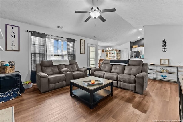 living room with a textured ceiling, visible vents, lofted ceiling, ceiling fan with notable chandelier, and wood finished floors