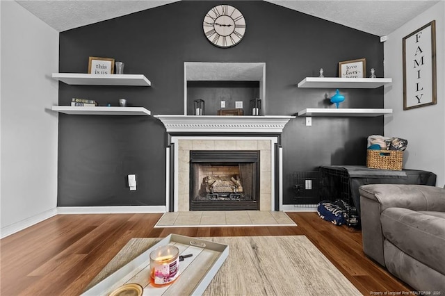 living room featuring baseboards, vaulted ceiling, a fireplace, a textured ceiling, and wood finished floors