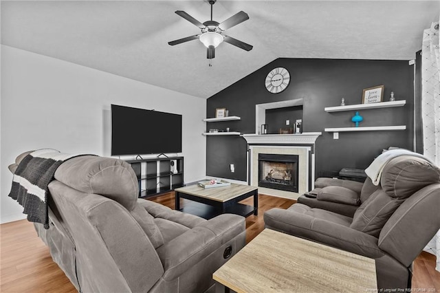 living area with wood finished floors, ceiling fan, lofted ceiling, and a tile fireplace