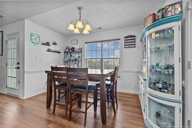 dining space featuring visible vents, a chandelier, wood finished floors, and a textured ceiling