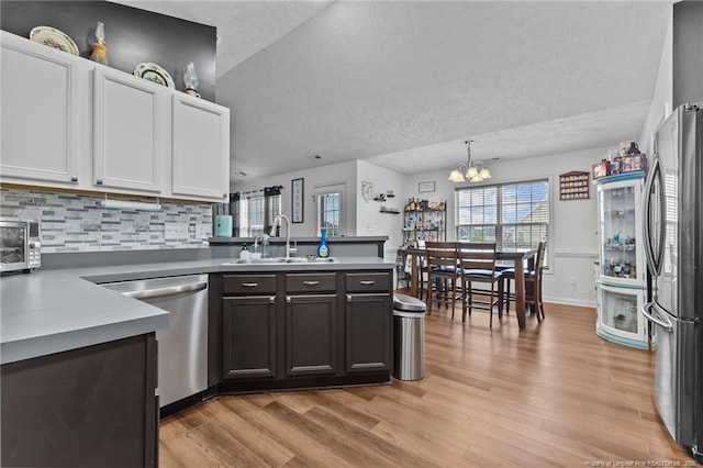 kitchen featuring a peninsula, a textured ceiling, light wood-style floors, stainless steel appliances, and a sink