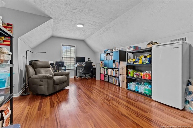 office space featuring visible vents, lofted ceiling, wood finished floors, and a textured ceiling