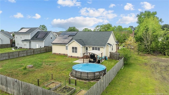 back of property featuring a vegetable garden, crawl space, a fenced backyard, a lawn, and solar panels