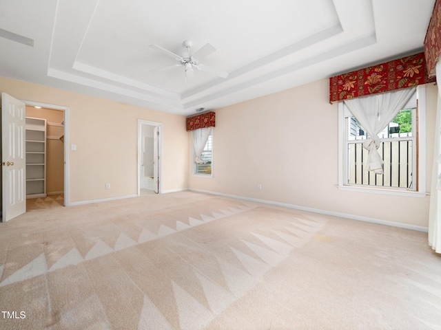 unfurnished bedroom with a tray ceiling, light colored carpet, baseboards, and a spacious closet