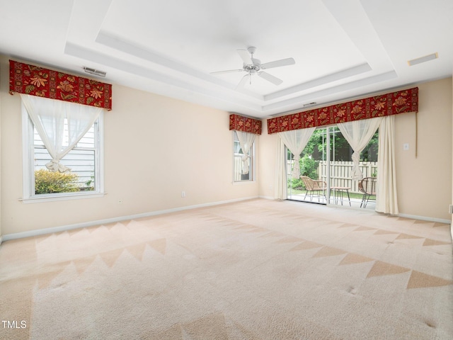 empty room with a raised ceiling, carpet floors, ceiling fan, and baseboards