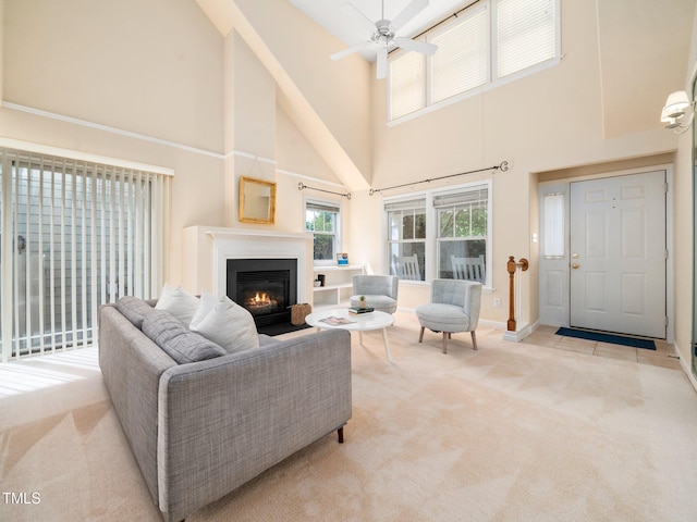 living room featuring a towering ceiling, light carpet, a lit fireplace, a ceiling fan, and baseboards