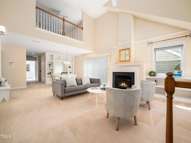 living area featuring light colored carpet, high vaulted ceiling, a lit fireplace, a chandelier, and baseboards