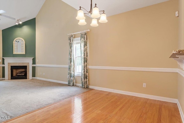 unfurnished living room with baseboards, vaulted ceiling, a fireplace with flush hearth, and wood finished floors