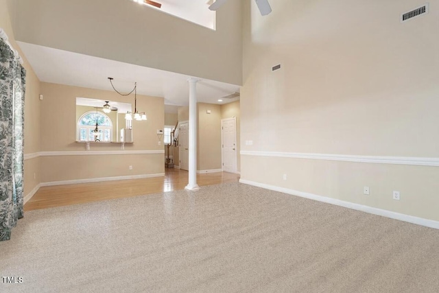 empty room with baseboards, visible vents, ornate columns, and ceiling fan with notable chandelier