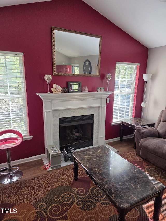 living area featuring lofted ceiling, a high end fireplace, wood finished floors, and baseboards