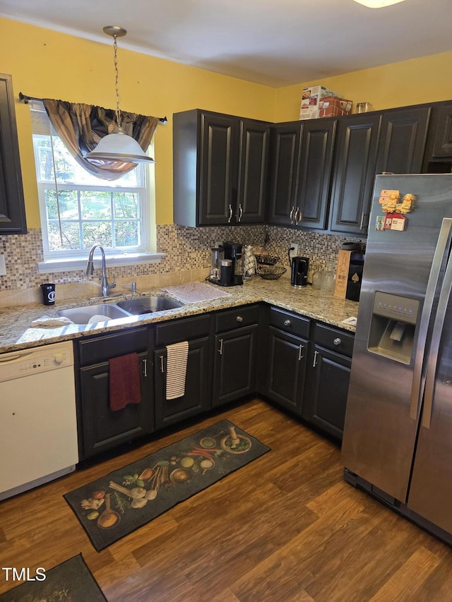 kitchen featuring stainless steel refrigerator with ice dispenser, white dishwasher, tasteful backsplash, dark cabinets, and a sink