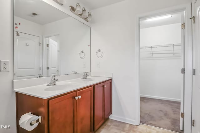 bathroom featuring a sink, a spacious closet, double vanity, baseboards, and visible vents