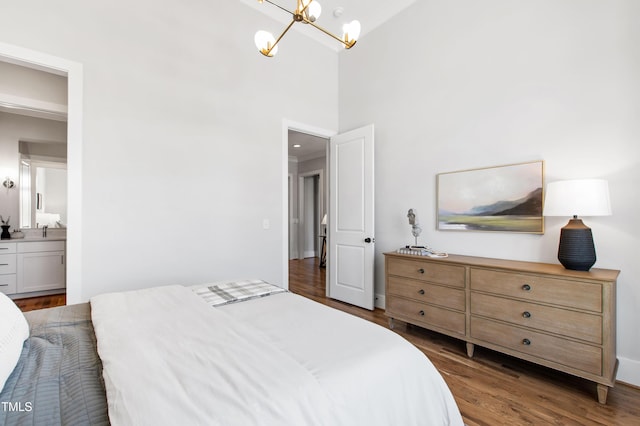 bedroom with ensuite bathroom, wood finished floors, a sink, an inviting chandelier, and a high ceiling