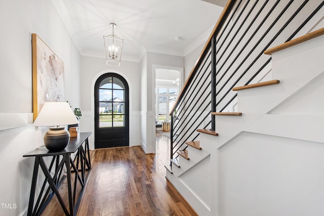 foyer with arched walkways, a chandelier, wood finished floors, stairway, and crown molding