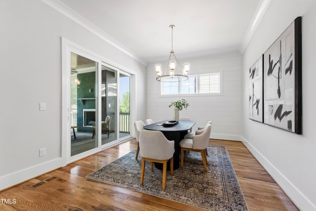 dining space featuring a chandelier, wood finished floors, visible vents, and crown molding