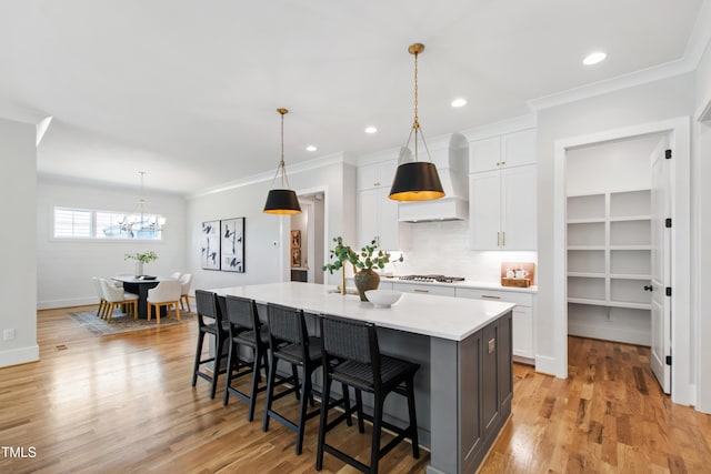 kitchen featuring white cabinets, an island with sink, light countertops, wall chimney range hood, and tasteful backsplash
