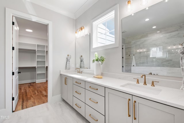 bathroom with a tile shower, ornamental molding, a sink, and double vanity