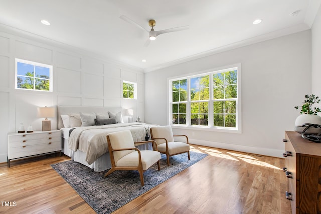 bedroom featuring crown molding, light wood-type flooring, baseboards, recessed lighting, and a decorative wall