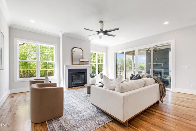 living area with baseboards, a ceiling fan, a glass covered fireplace, and ornamental molding