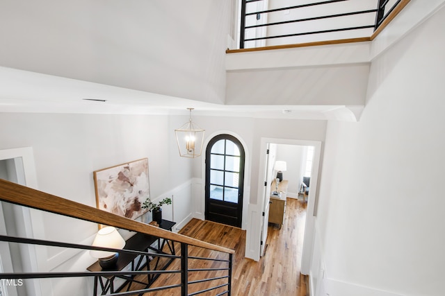 foyer entrance with a high ceiling, a notable chandelier, a wainscoted wall, and light wood-style flooring