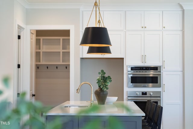 kitchen featuring white cabinets, hanging light fixtures, a sink, and light countertops