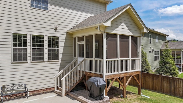 rear view of property featuring fence, a sunroom, a shingled roof, and a patio