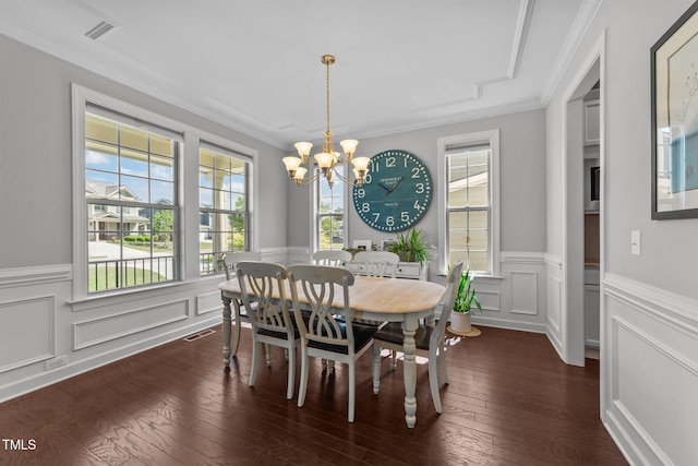dining area featuring a chandelier, wainscoting, dark wood-style flooring, crown molding, and a decorative wall