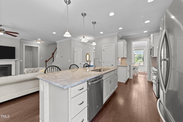 kitchen with stainless steel appliances, a sink, open floor plan, a ceiling fan, and white cabinetry
