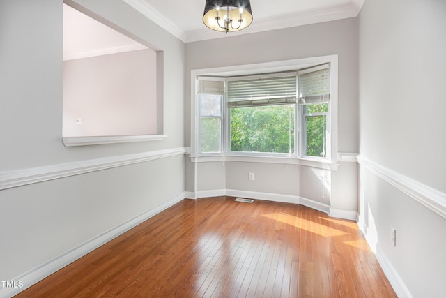 empty room with baseboards, an inviting chandelier, crown molding, visible vents, and wood-type flooring