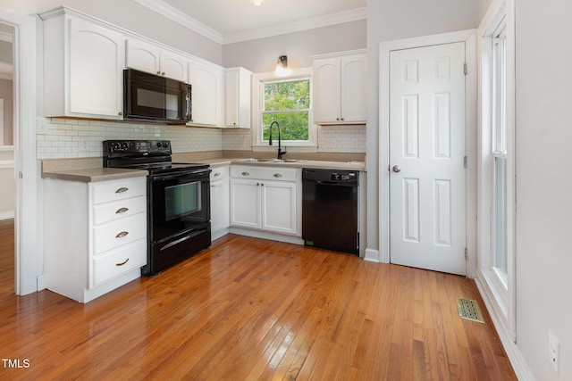 kitchen with visible vents, white cabinets, a sink, black appliances, and light wood-style flooring