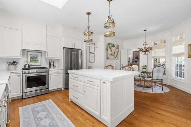 kitchen with appliances with stainless steel finishes, a chandelier, ornamental molding, white cabinetry, and pendant lighting