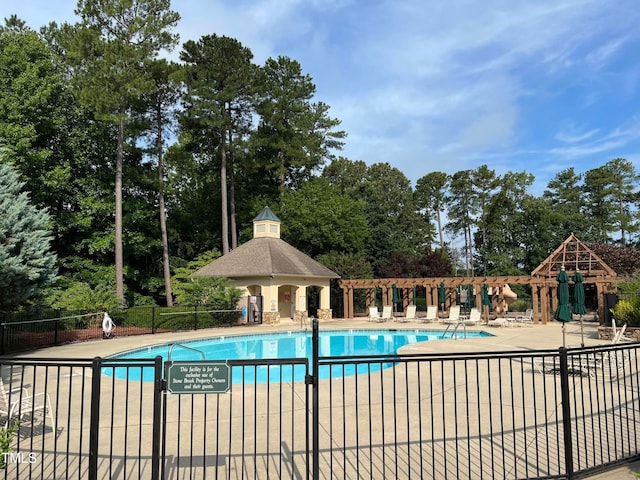community pool with fence, view of wooded area, and a patio