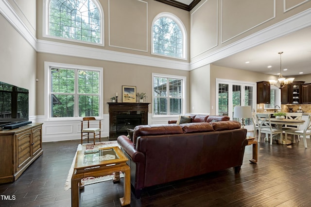living area featuring a chandelier, a glass covered fireplace, a decorative wall, a high ceiling, and wainscoting