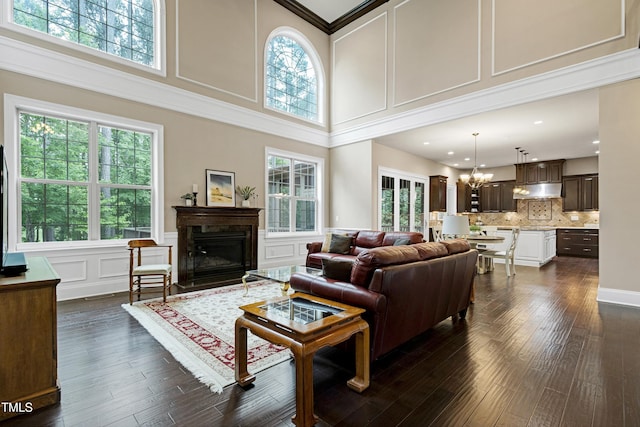 living room featuring a high ceiling, a chandelier, dark wood-style flooring, a decorative wall, and a glass covered fireplace
