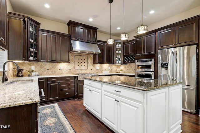 kitchen with stainless steel appliances, a sink, under cabinet range hood, dark brown cabinets, and a kitchen island