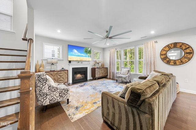 living area featuring a glass covered fireplace, a ceiling fan, recessed lighting, wood finished floors, and stairway