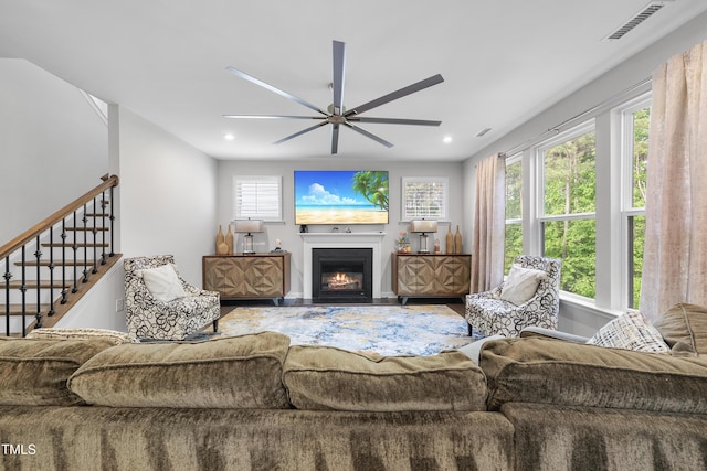 living area featuring visible vents, a glass covered fireplace, ceiling fan, and a wealth of natural light
