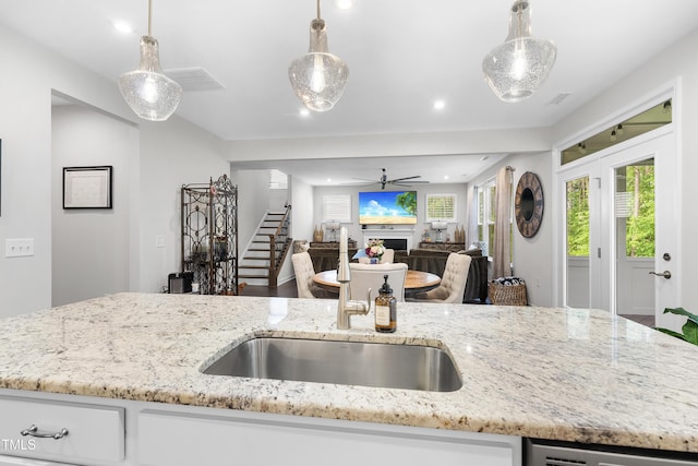 kitchen featuring light stone counters, hanging light fixtures, a sink, a ceiling fan, and open floor plan