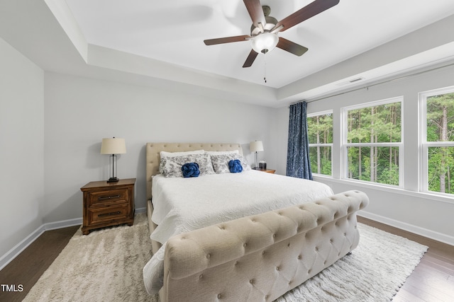 bedroom featuring visible vents, wood finished floors, baseboards, a raised ceiling, and a ceiling fan