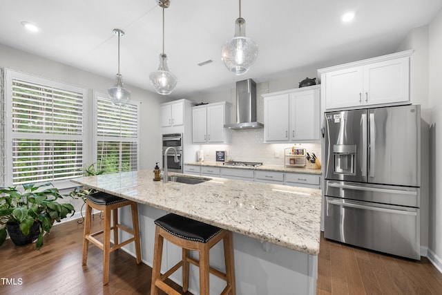 kitchen featuring appliances with stainless steel finishes, a center island with sink, a sink, white cabinets, and wall chimney exhaust hood