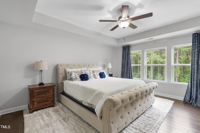 bedroom with a raised ceiling, baseboards, wood-type flooring, and ceiling fan