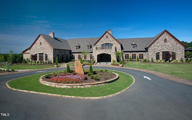 view of front of home featuring curved driveway, a chimney, stone siding, and a front lawn