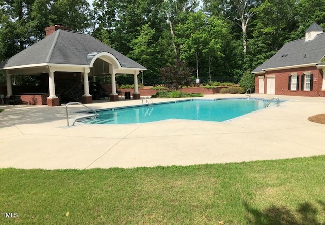 community pool with a gazebo, a patio area, view of wooded area, and a lawn