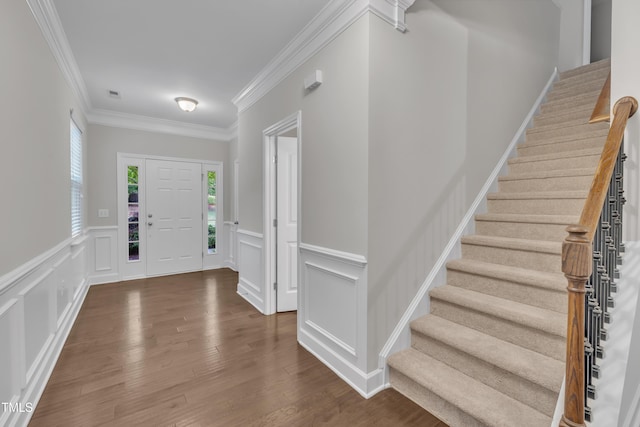entryway featuring a decorative wall, stairway, crown molding, wainscoting, and wood finished floors