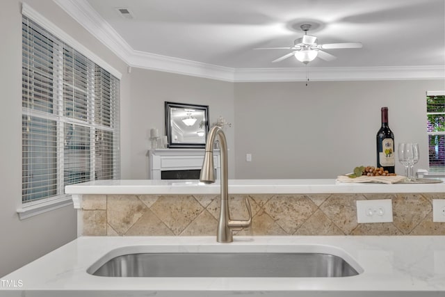 kitchen with a sink, ceiling fan, crown molding, and light countertops