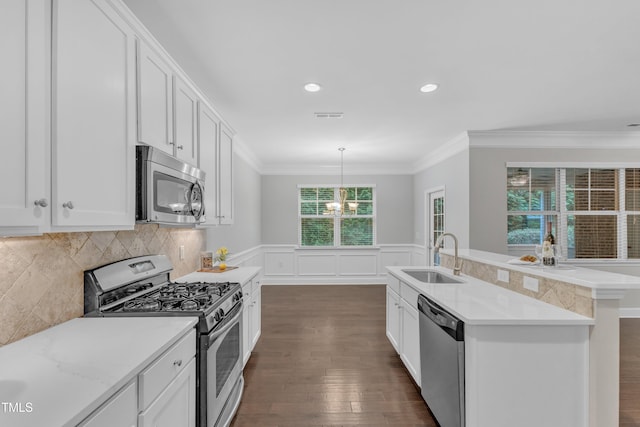 kitchen featuring appliances with stainless steel finishes, a sink, a chandelier, a wainscoted wall, and white cabinets