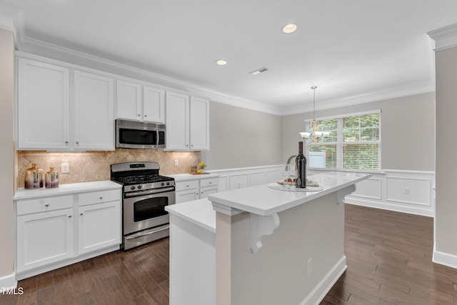 kitchen with appliances with stainless steel finishes, dark wood-style flooring, light countertops, white cabinetry, and ornamental molding